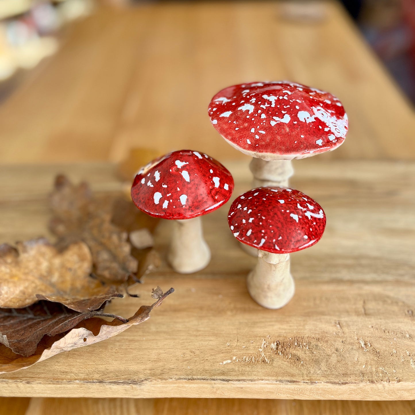 Three red and white mushroom-shaped ornaments on a wooden surface with blurred background