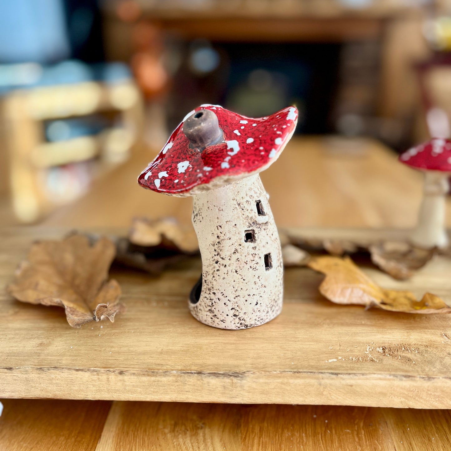 Small ceramic mushroom figurine from the side view with a red cap on a wooden surface