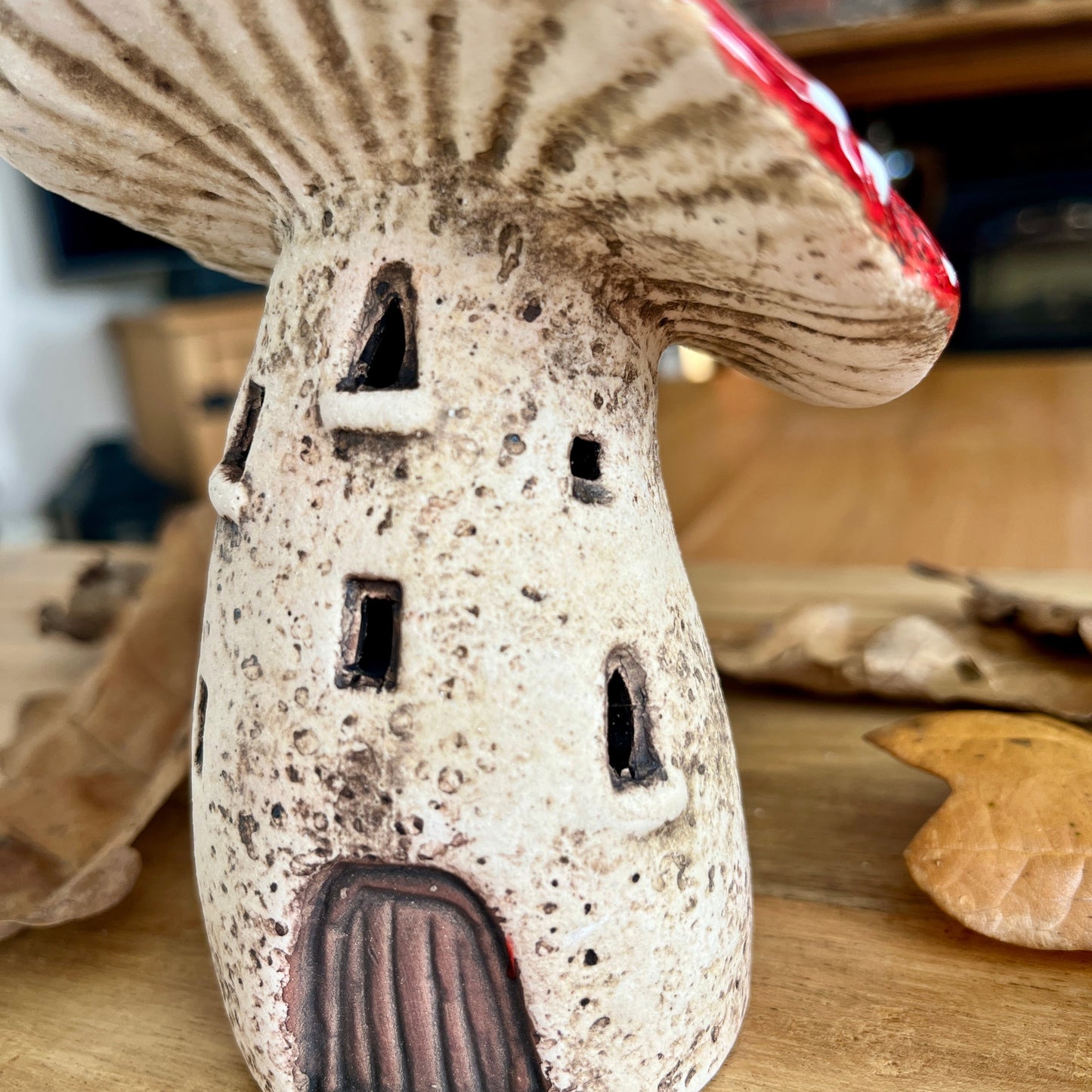 Close up of a ceramic mushroom-shaped house from the side on a wooden surface with a blurred background