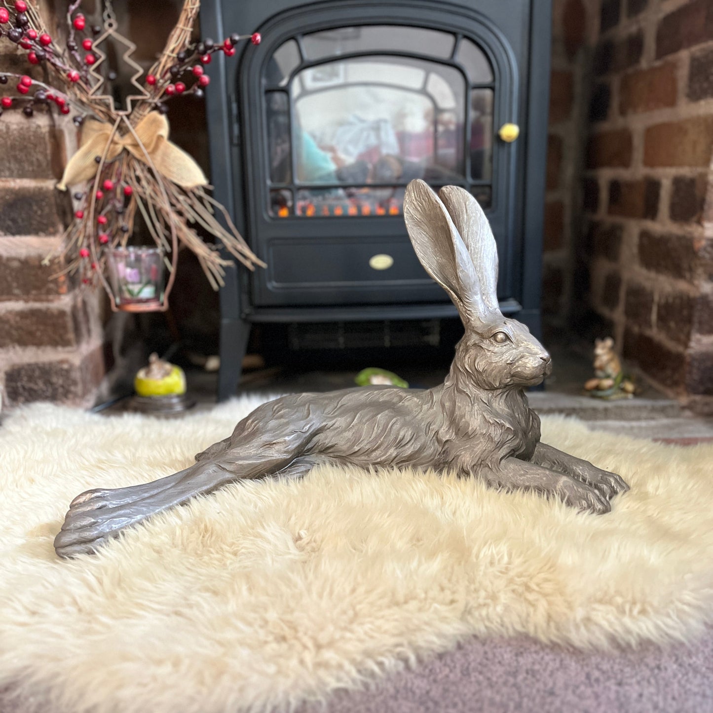 A hare figurine lying down in front of an electric fire on a sheepskin rug