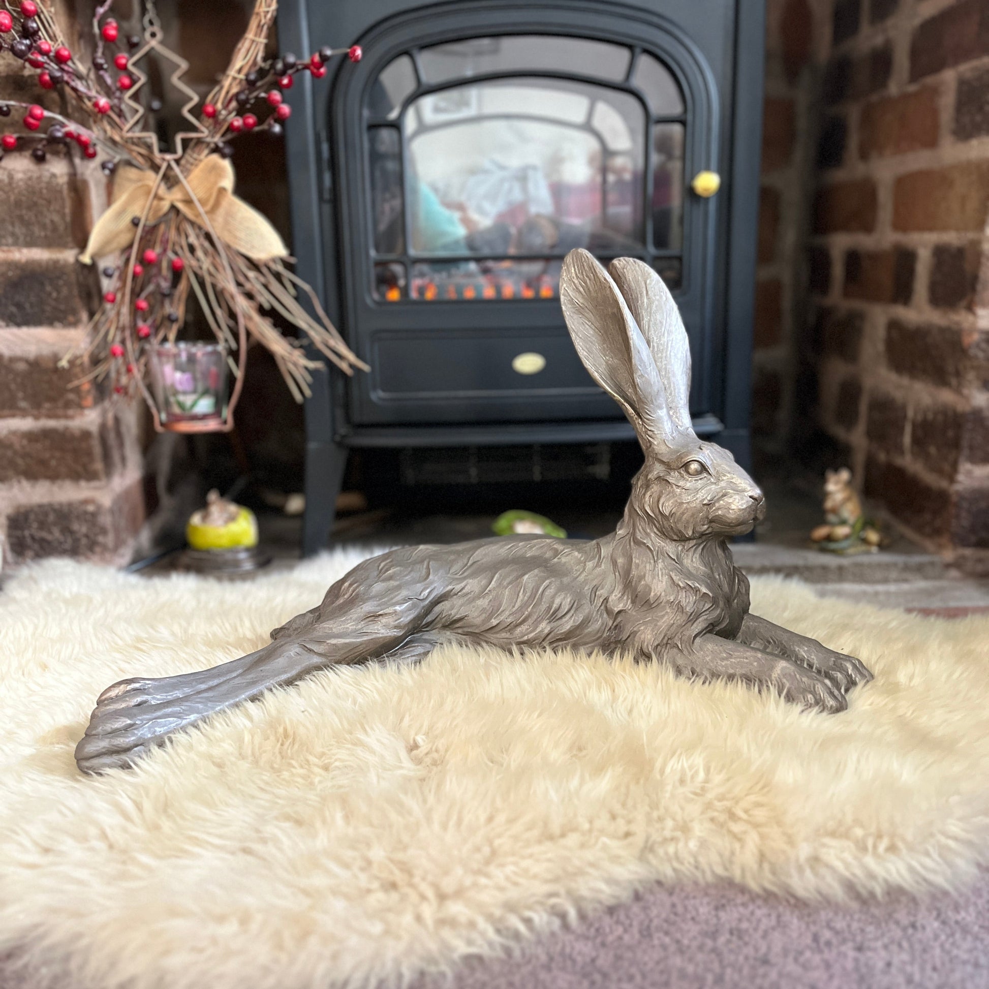 A hare figurine lying down in front of an electric fire on a sheepskin rug