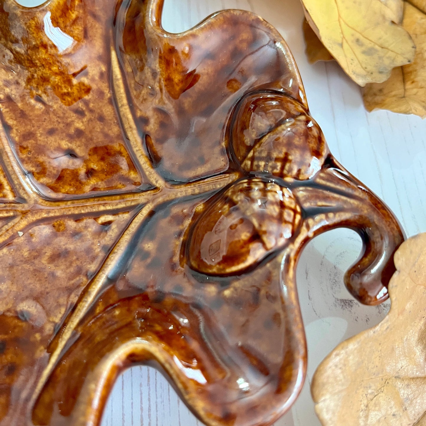 Close up of end of decorative leaf-shaped plate with a brown finish and embossed acorns on a light background