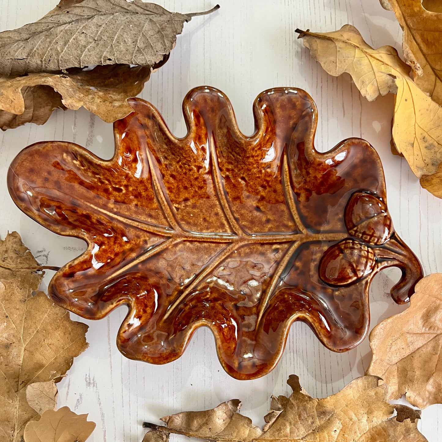 Decorative ceramic leaf with a glossy finish on a wooden surface with real leaves.