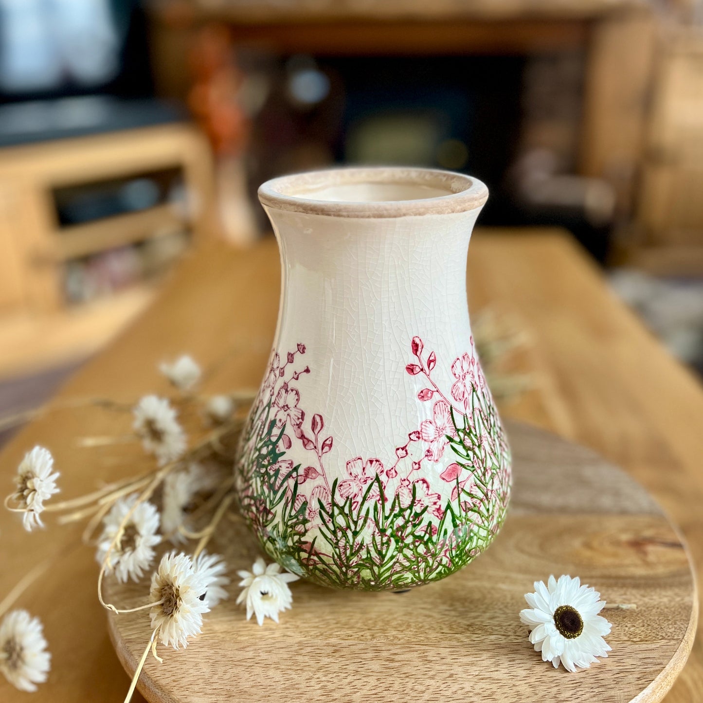 Decorative vase with floral patterns on a wooden surface with flowers around