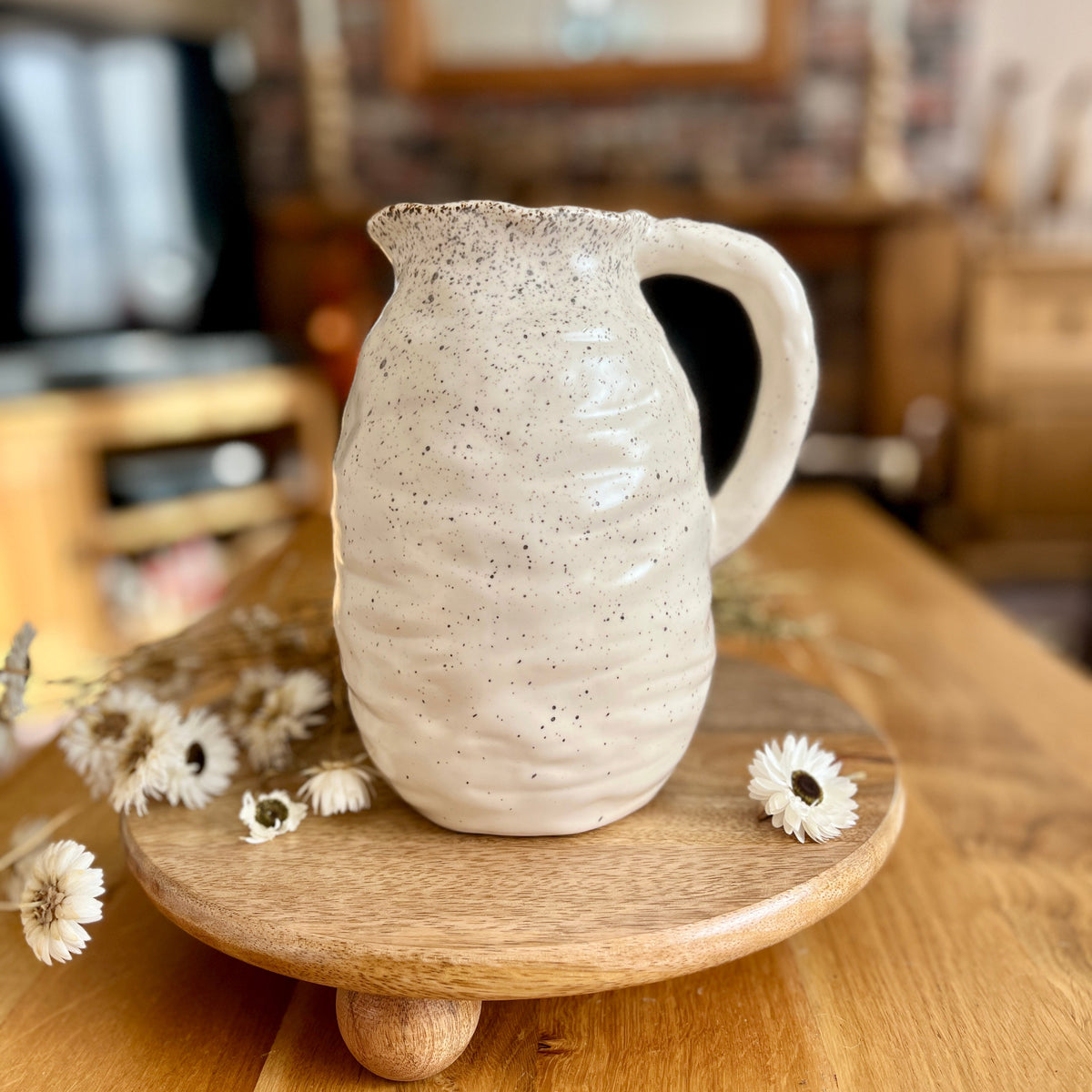 Ceramic speckled jug on a wooden stand with flowers on a wooden surface