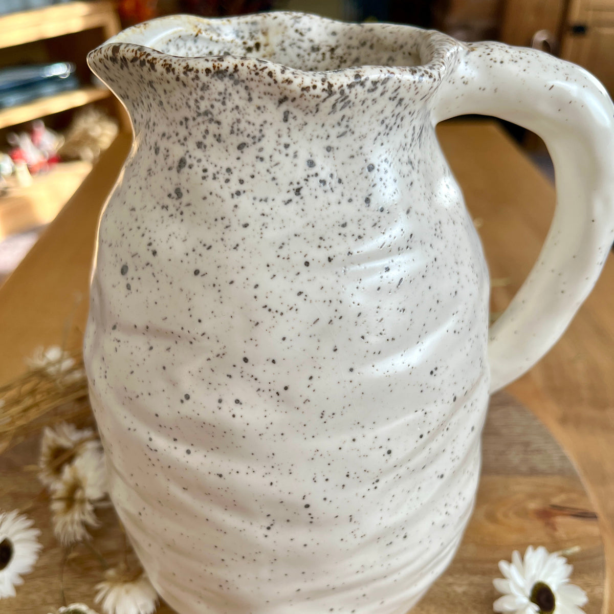 Speckled ceramic jug close up on a wooden surface with flowers