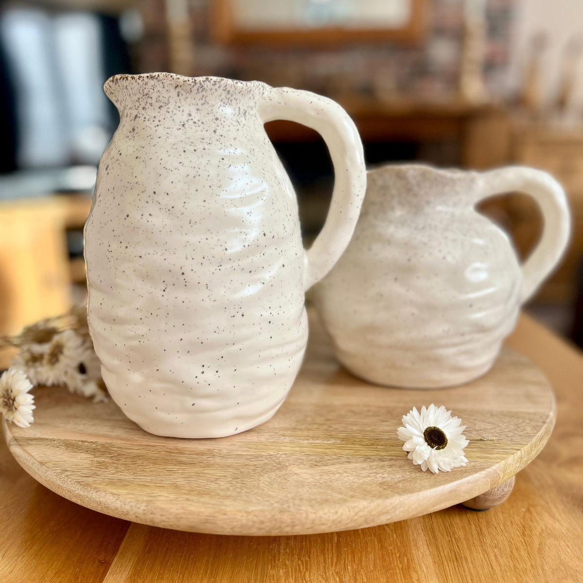 Two matching ceramic speckled jugs on a wooden tray with a blurred kitchen background