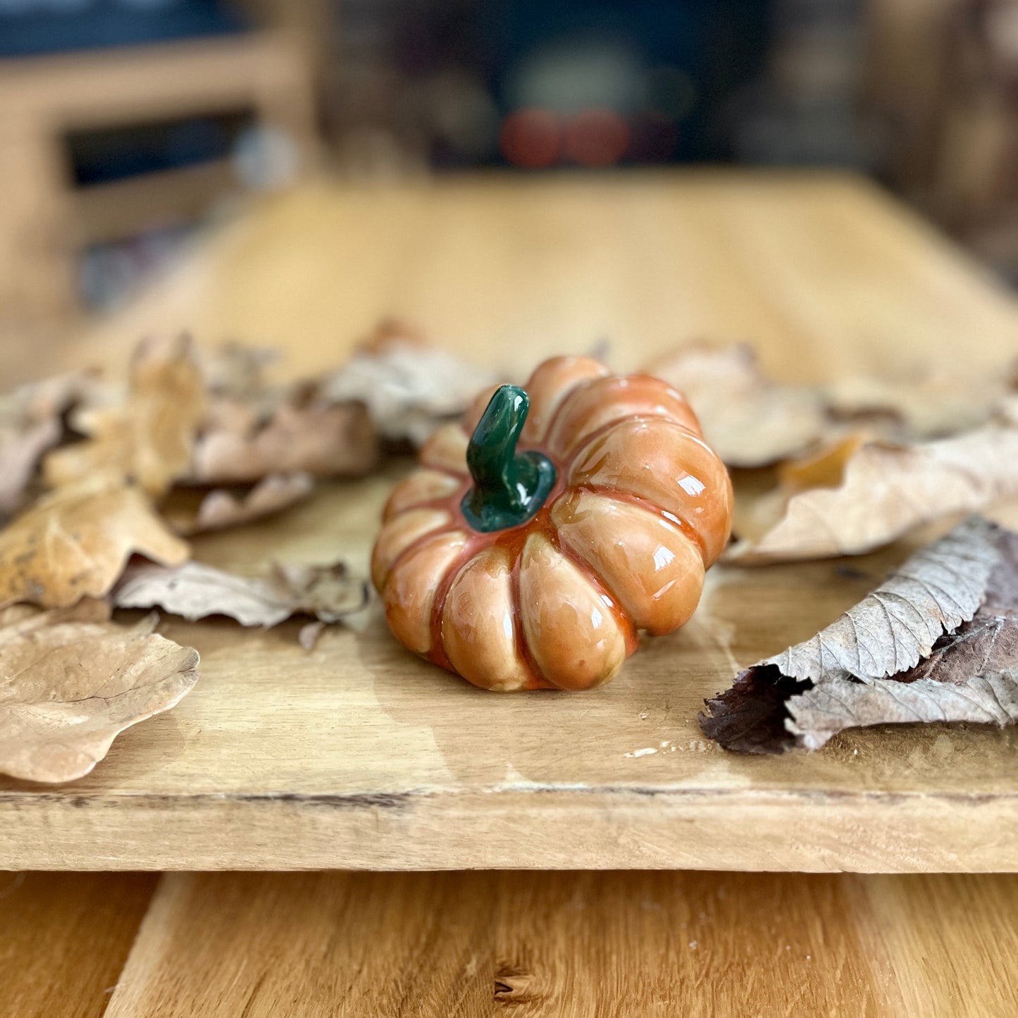 Small ceramic pumpkin on a wooden surface with dried leaves