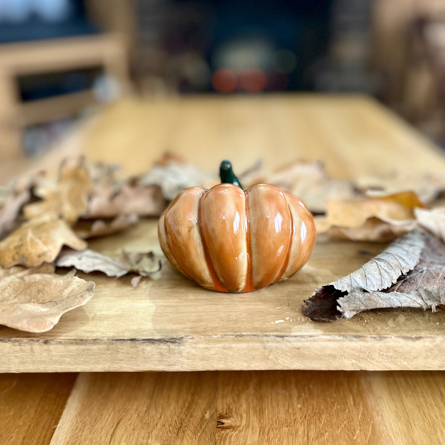 Small ceramic pumpkin on a wooden surface with dried leaves
