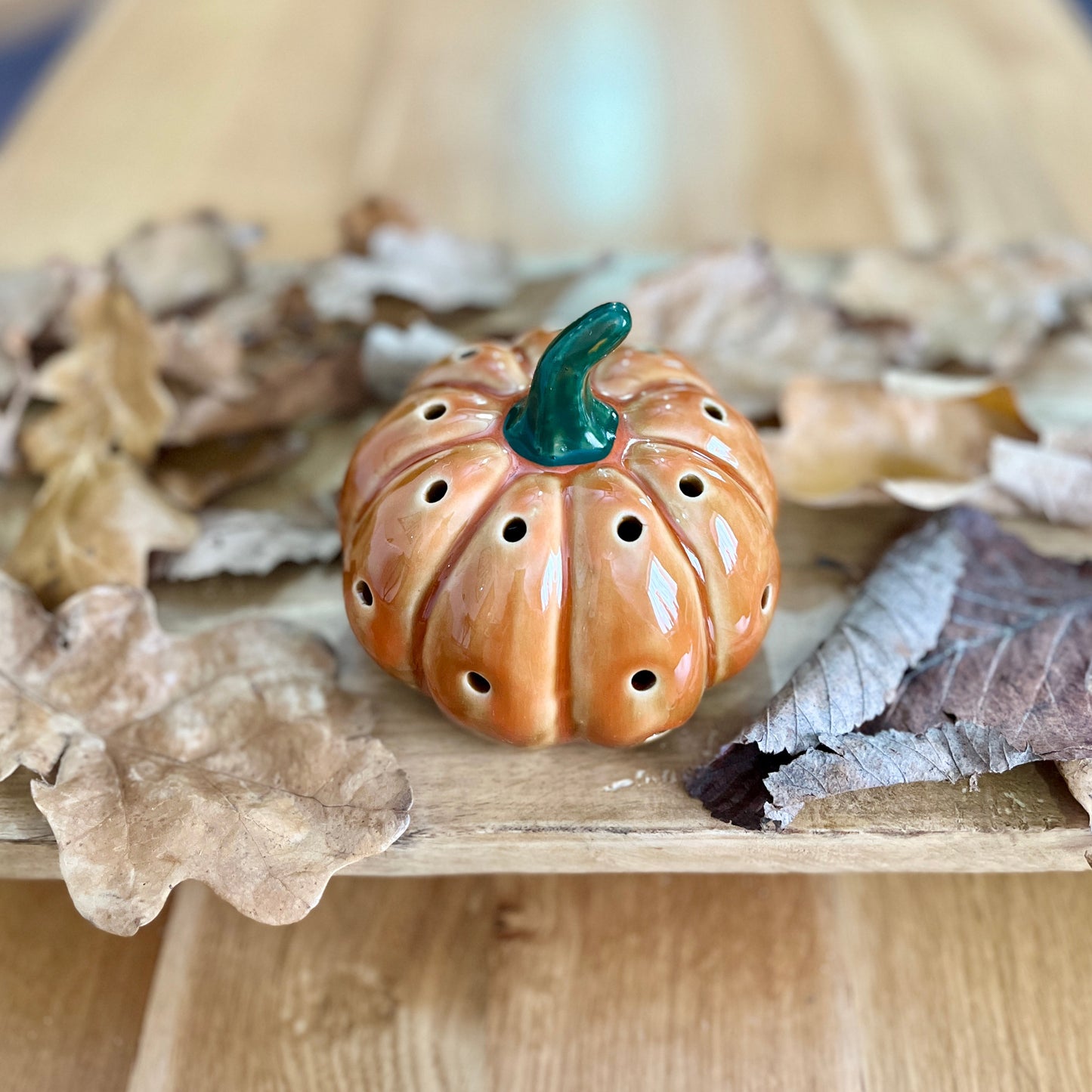 Ceramic pumpkin shaped decorative ornament on a wooden surface with leaves