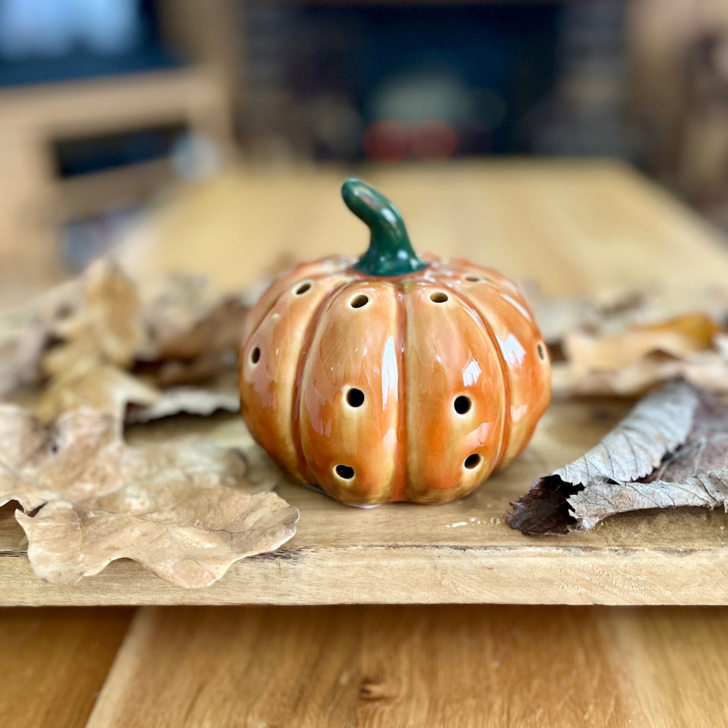 Decorative ceramic pumpkin with holes on a wooden surface with leaves