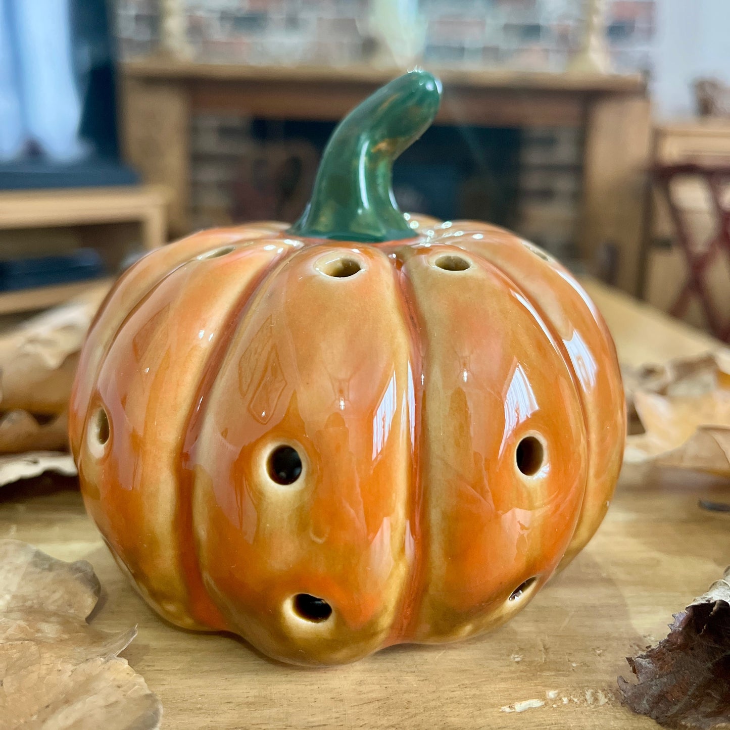 Ceramic pumpkin-shaped object with multiple holes on a wooden surface