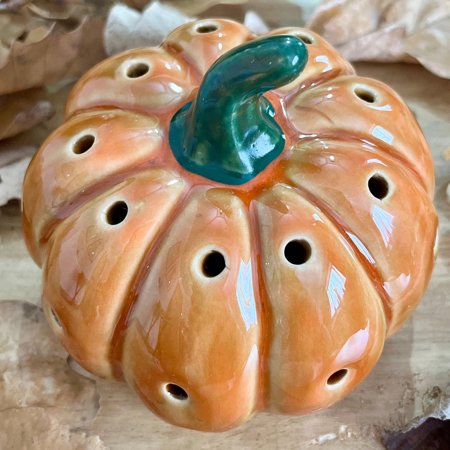 Ceramic pumpkin shaped decorative item with a green stem on a wooden surface.