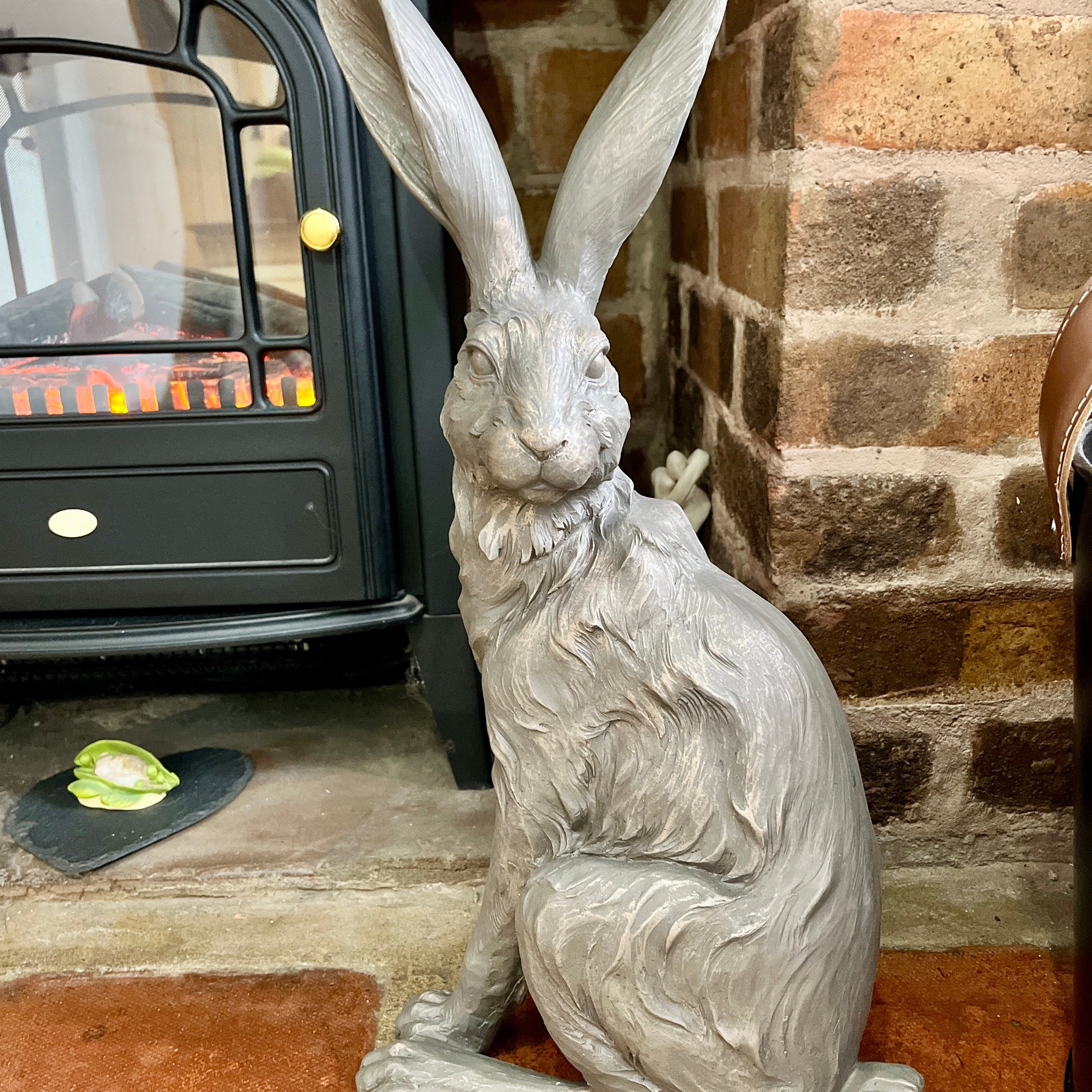 Statue of a hare in front of a fireplace with a brick wall background