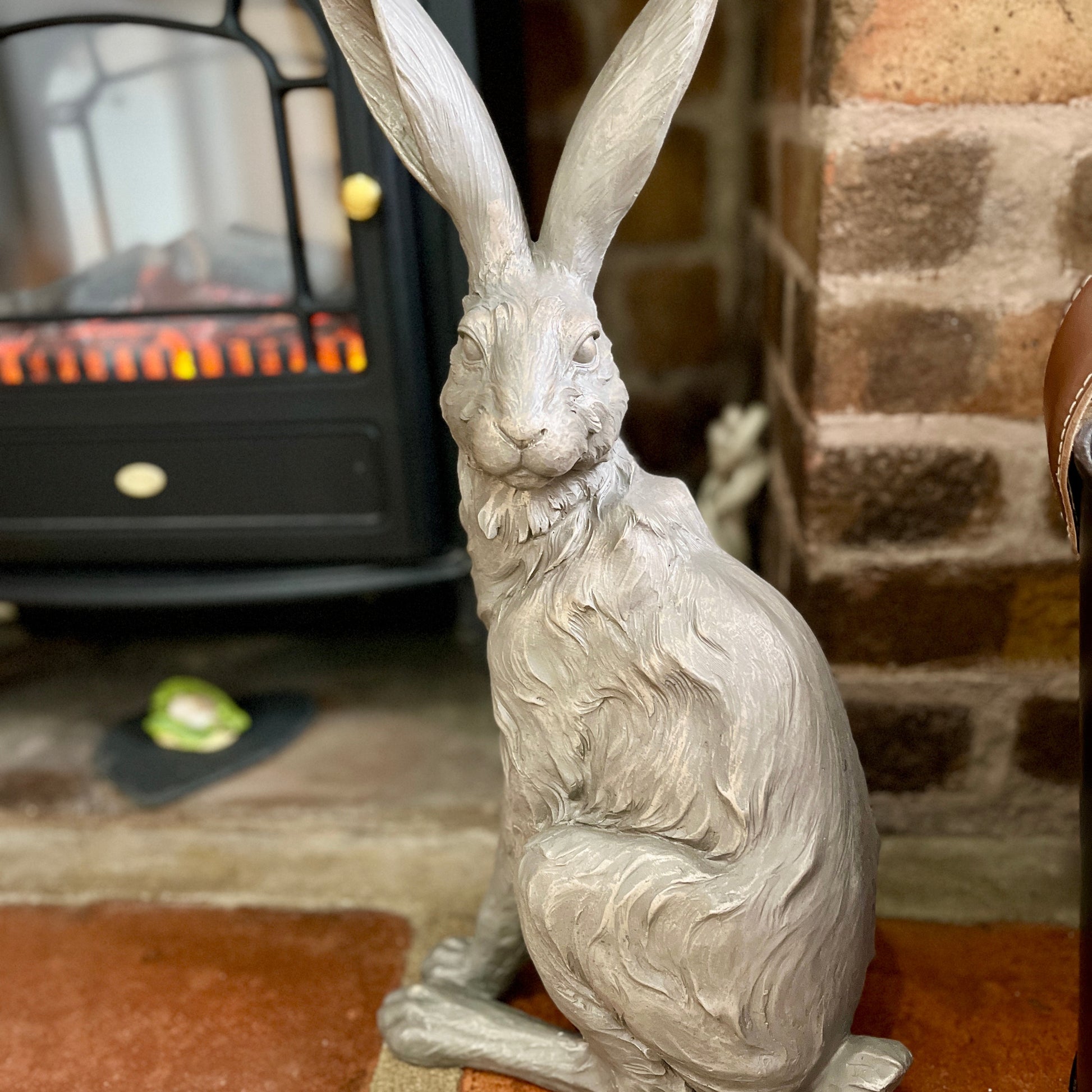 Statue of a hare in front of a fireplace with a brick wall background