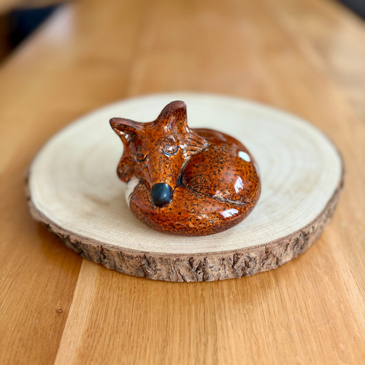 Ceramic sleeping fox figurine on a wooden base
