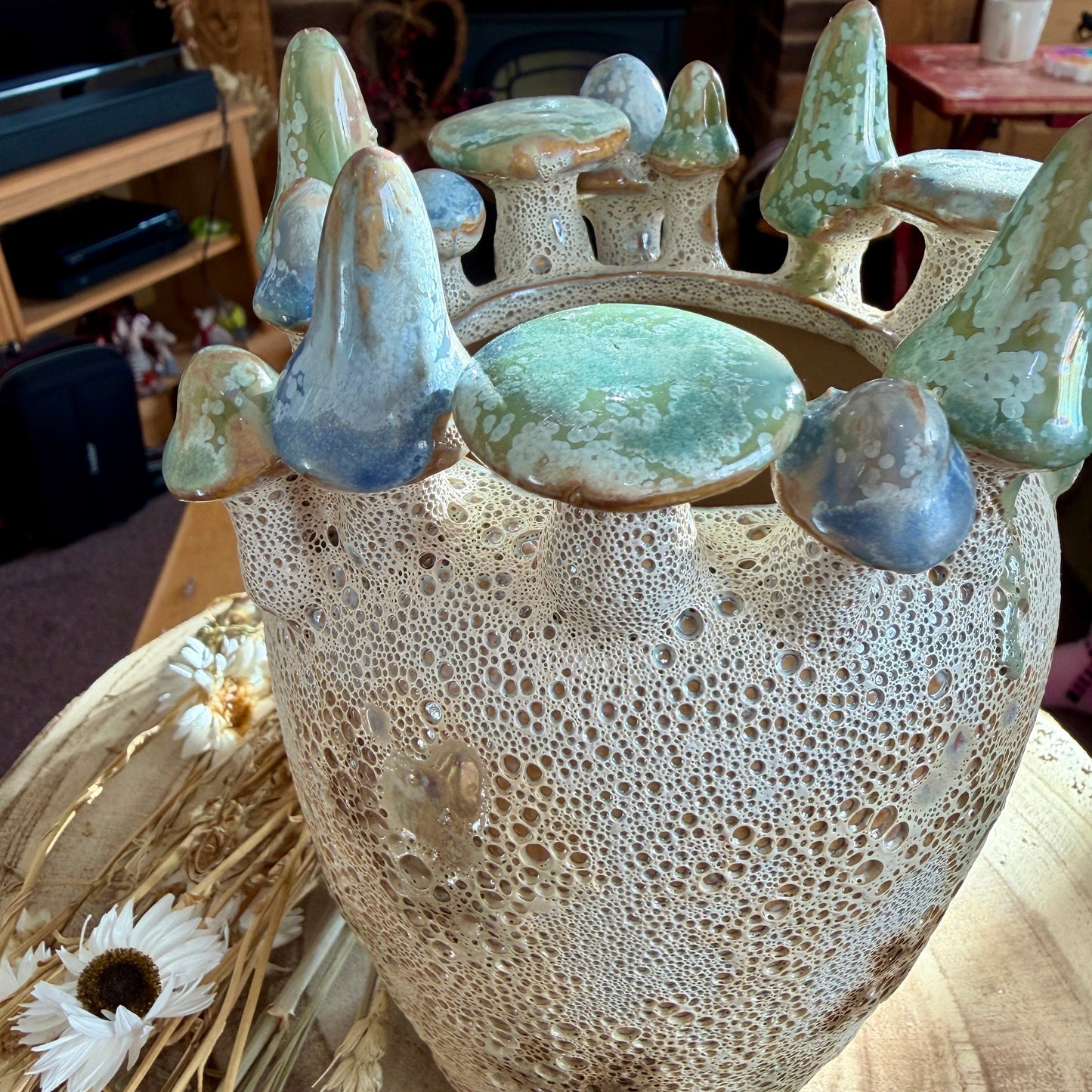 Ceramic vase with textured surface and decorative toadstools on a table with flowers.
