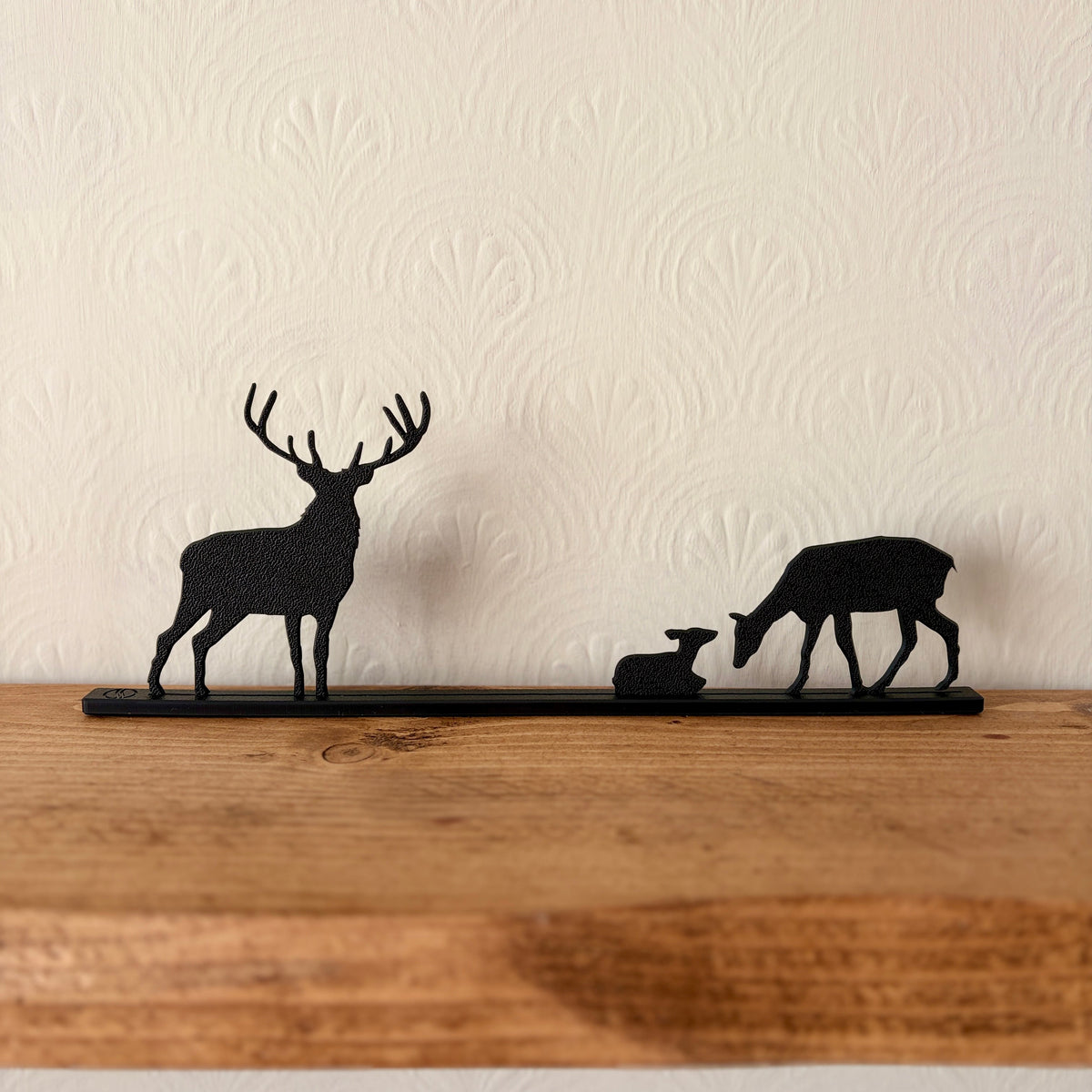Black recycled plastic deer silhouette shelf decor featuring a stag, a doe, and a fawn mounted on a wooden shelf against a cream patterned wall.