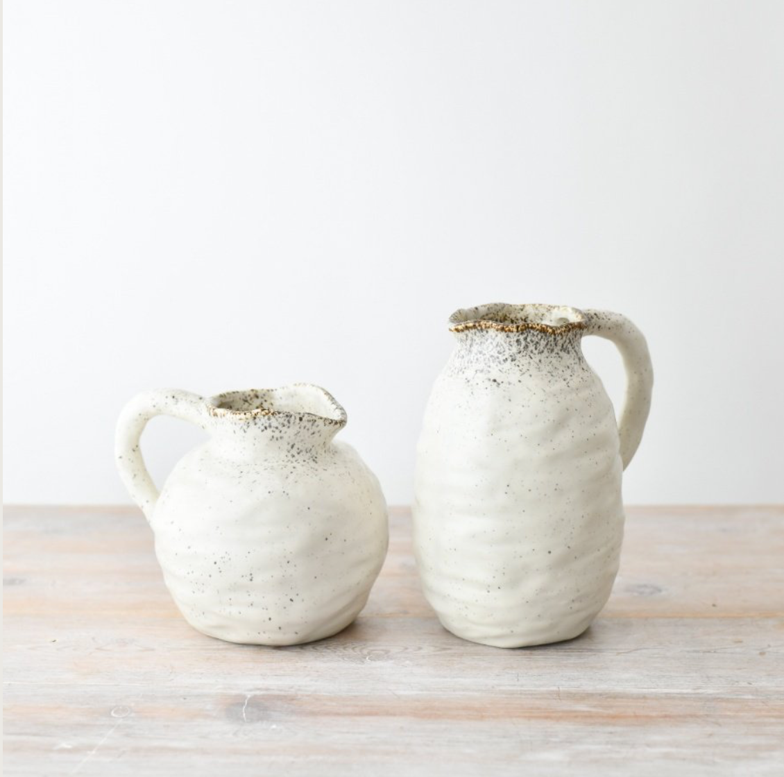 Matching ceramic pitchers on a wooden surface with a white background