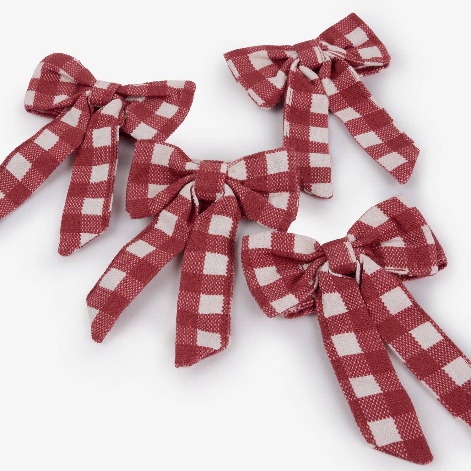 Four fabric ribbon bows in a red and white gingham checkered pattern, arranged on a light gray background.