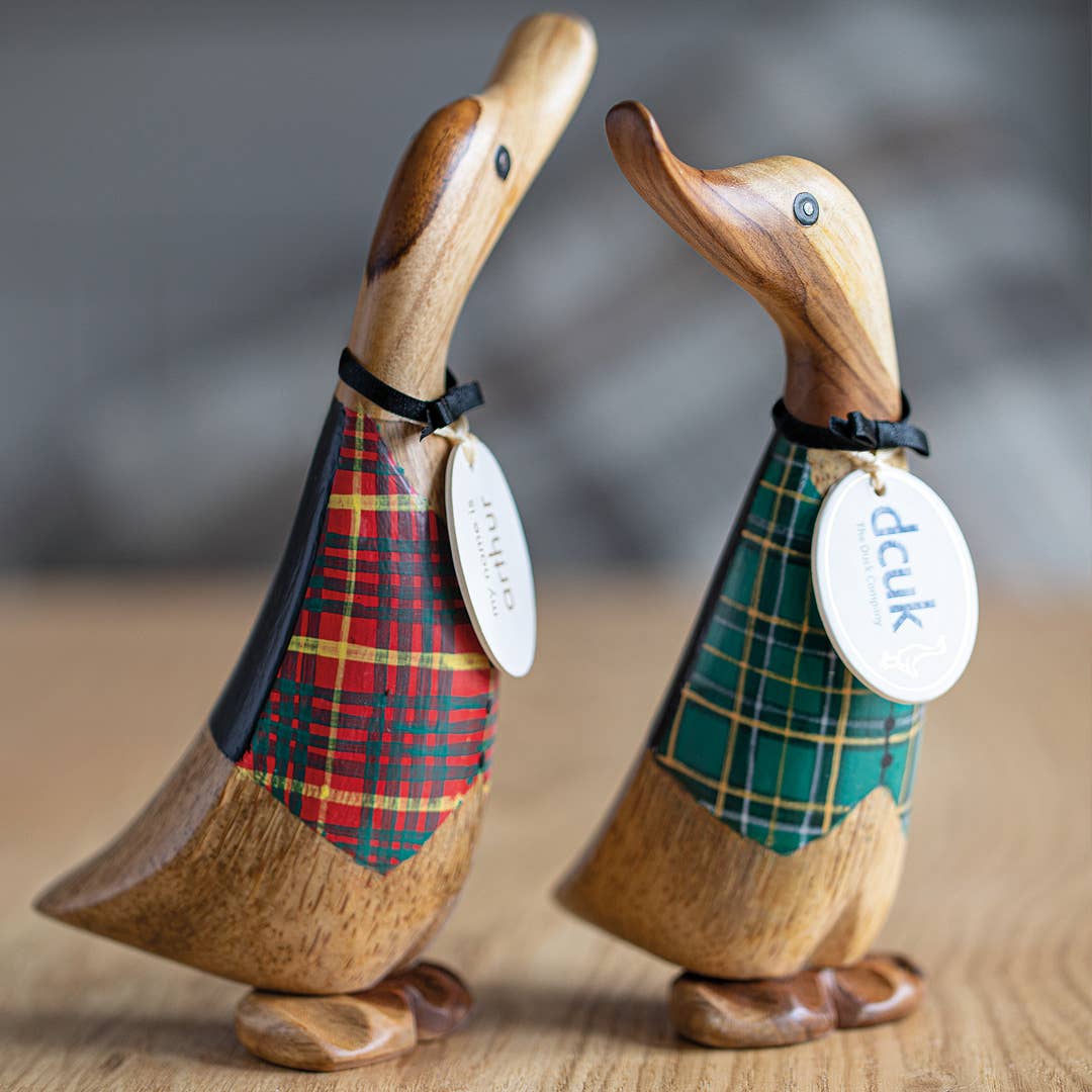 Two wooden duck figurines wearing plaid waistcoats with visible brand tags on a wooden surface.