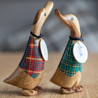 Two wooden duck figurines wearing plaid waistcoats with visible brand tags on a wooden surface.