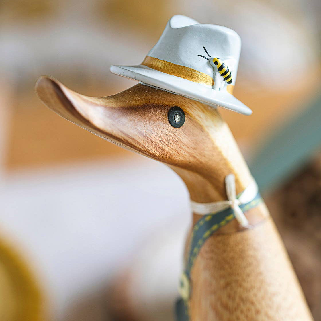 Wooden duck figure wearing a white hat with a bee design on a blurred background
