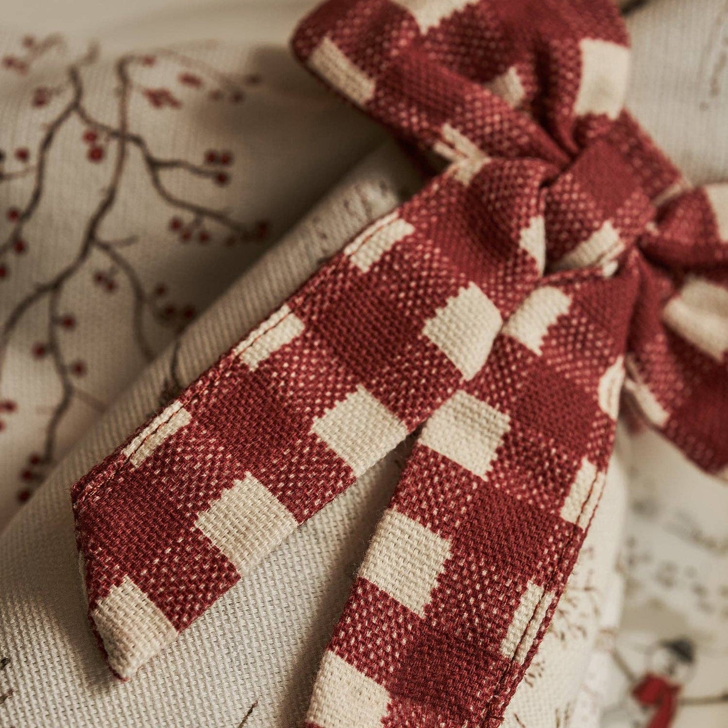 A close-up of a red and cream gingham checkered fabric bow tied over a beige patterned textile.