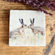 Image of a square marble coaster with watercolour painted hares nose to nose as though they are kissing.