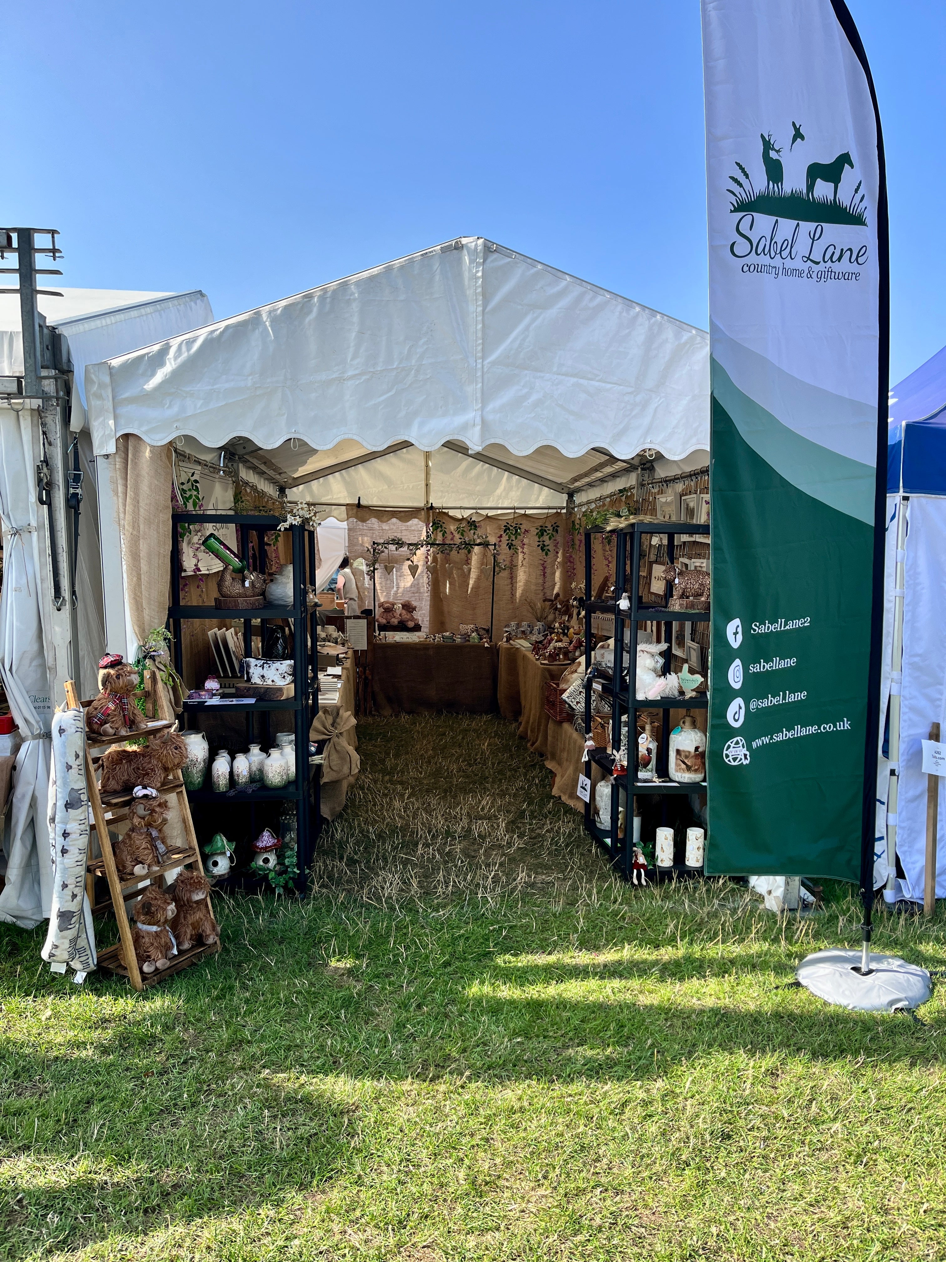 Outdoor market stall with products and a branded banner on a grassy area.