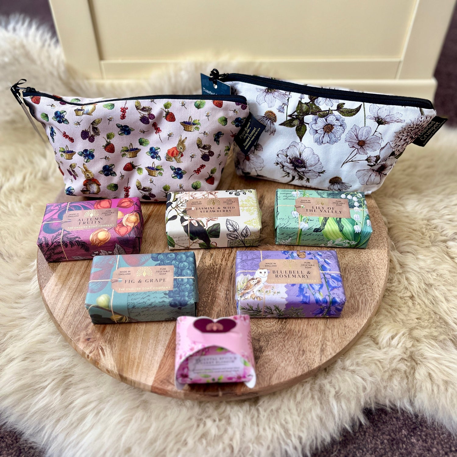 Set of floral-patterned make up bags and soap bars on a wooden board with a fur surface underneath.