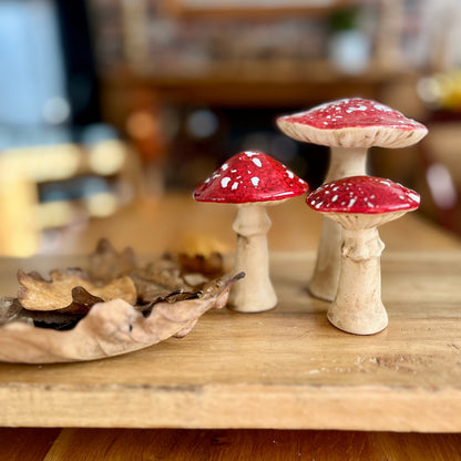Three decorative mushrooms with red caps and white spots on a wooden surface.