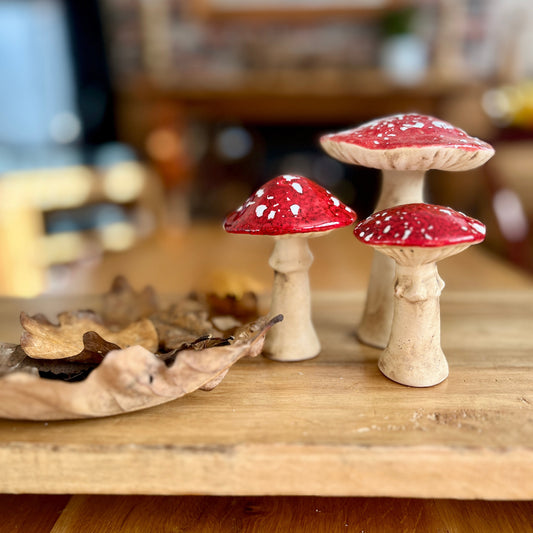 Three decorative mushrooms with red caps and white spots on a wooden surface.