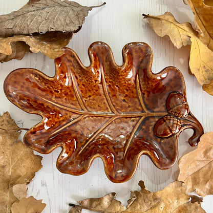 Decorative ceramic leaf with a glossy finish on a wooden surface with real leaves.