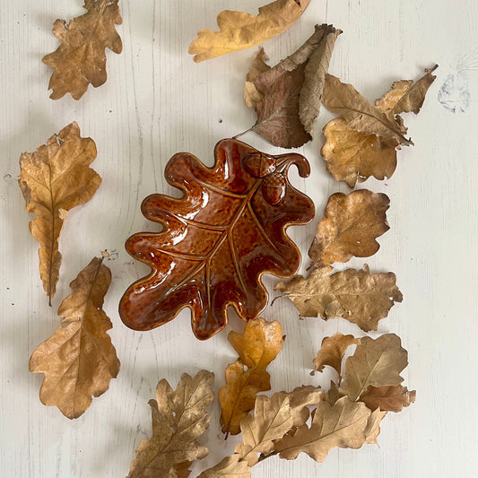 Decorative ceramic leaf on a white wooden surface with other leaves.