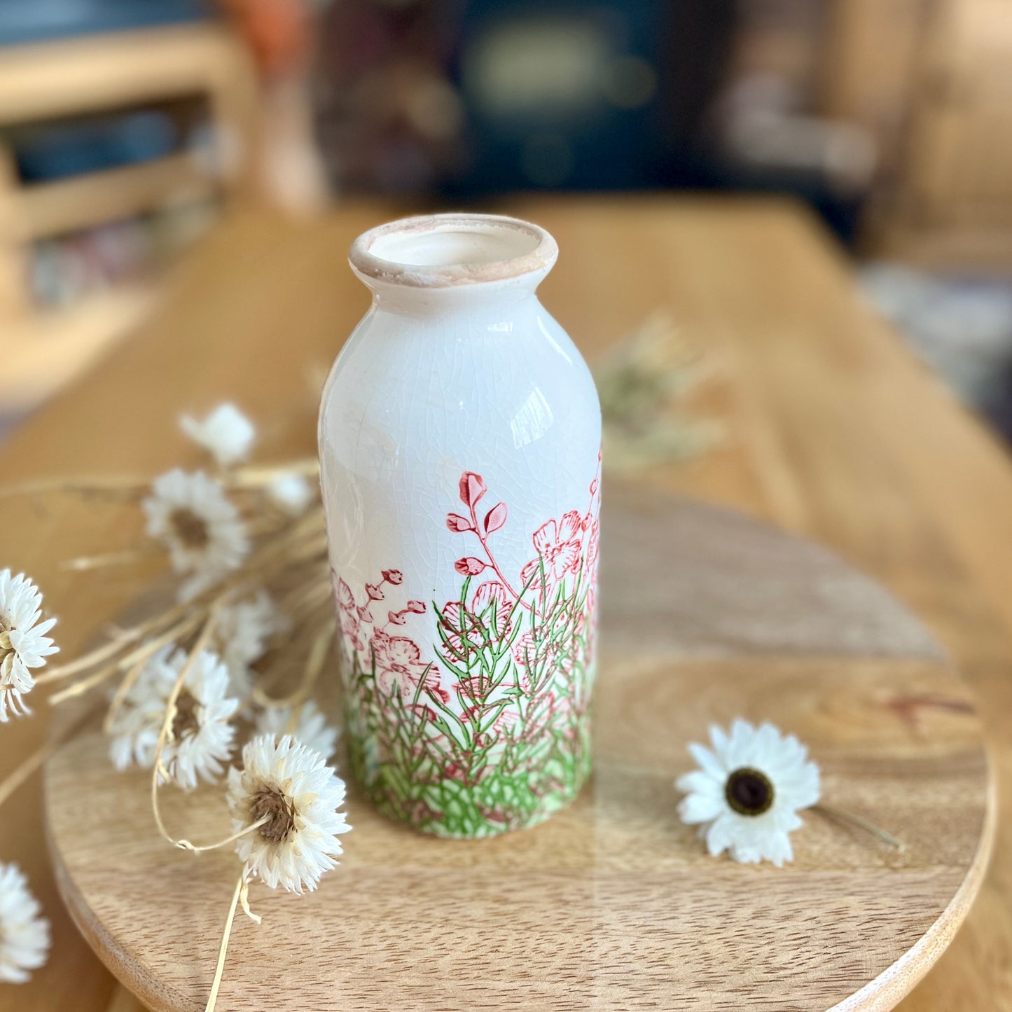 White bottle shaped vase with floral design on a wooden surface with dried flowers