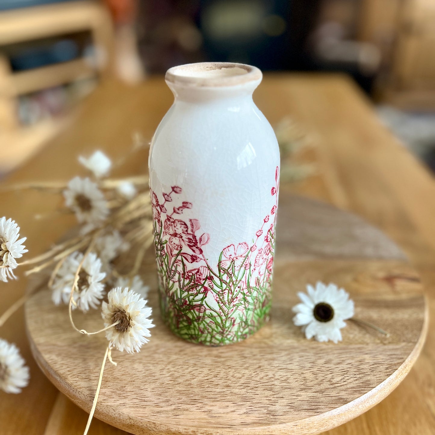 Decorative bottle shaped vase with floral design on a wooden stand with flowers around