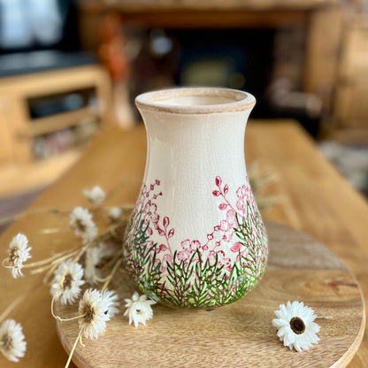Decorative vase with floral patterns on a wooden surface with flowers around