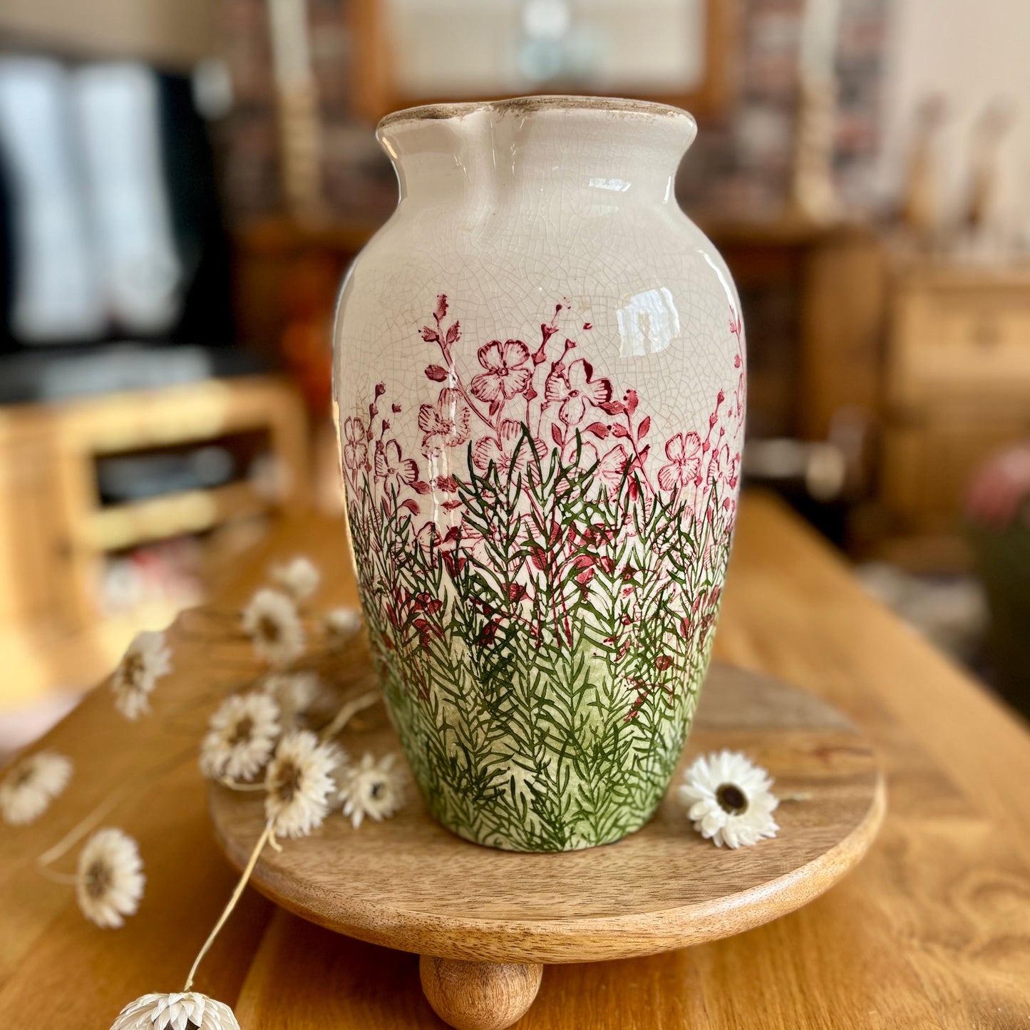 Decorative vase with floral design on a wooden stand, surrounded by dried flowers.