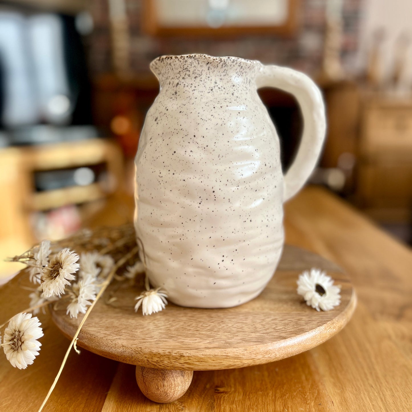 Ceramic speckled jug on a wooden stand with dried flowers on a wooden surface