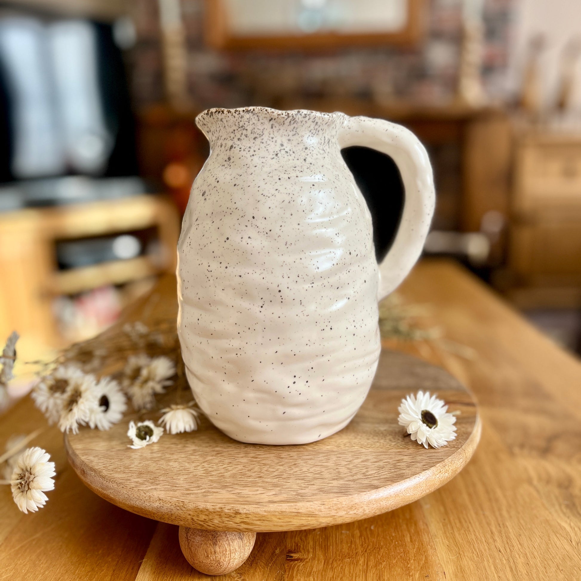 Ceramic speckled jug on a wooden stand with flowers on a wooden surface