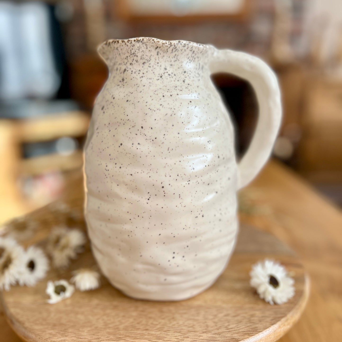 Speckled ceramic jug on a wooden stand with blurred background