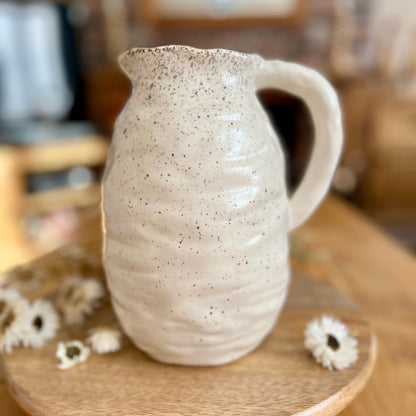 Speckled ceramic jug on a wooden stand with blurred background