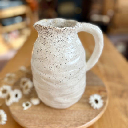 Speckled ceramic jug on a wooden surface with blurred background