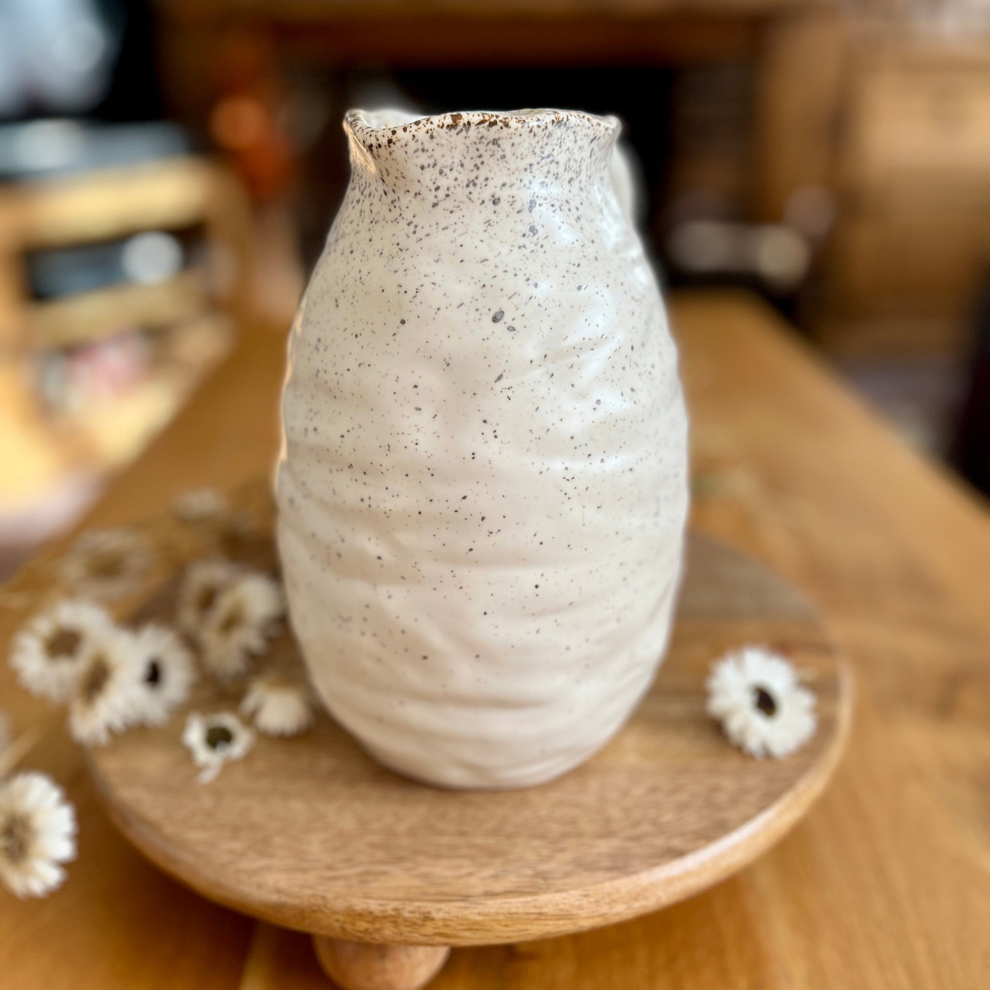 Speckled ceramic vase on a wooden stand with dried flowers on a wooden surface