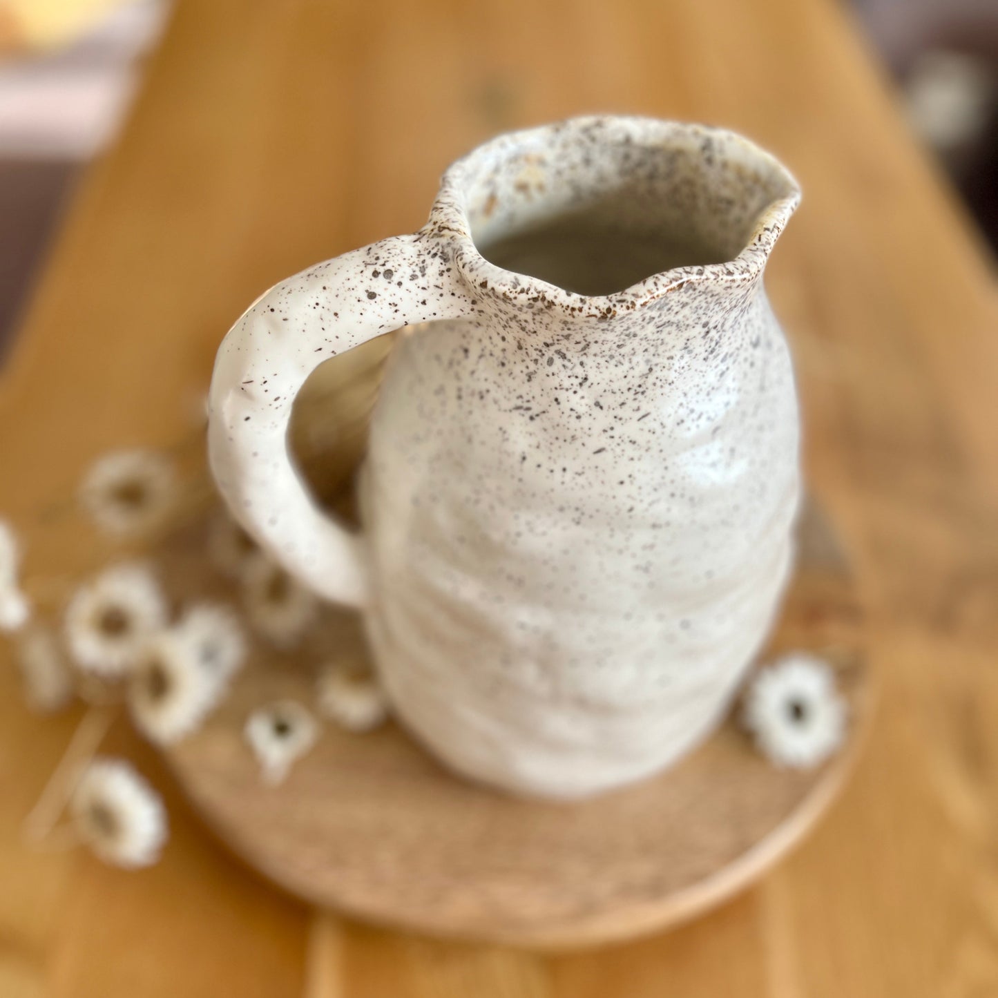 Speckled ceramic jug on a wooden surface with scattered items.
