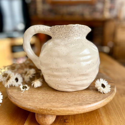 White ceramic jug on a wooden stand with flowers on a wooden surface