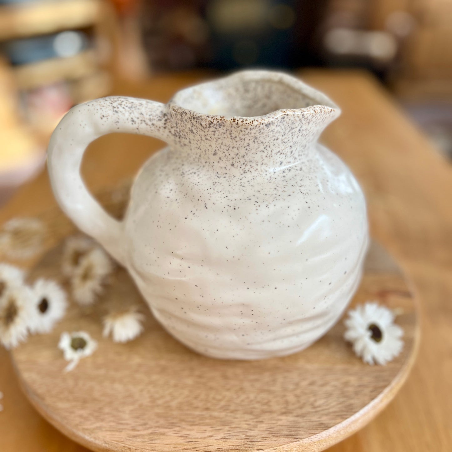 Speckled ceramic jug on a wooden surface with blurred background