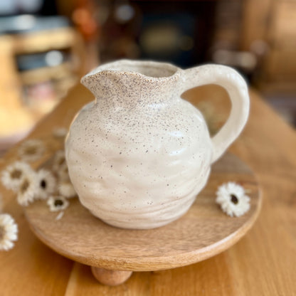 Speckled ceramic jug on a wooden stand with a blurred background