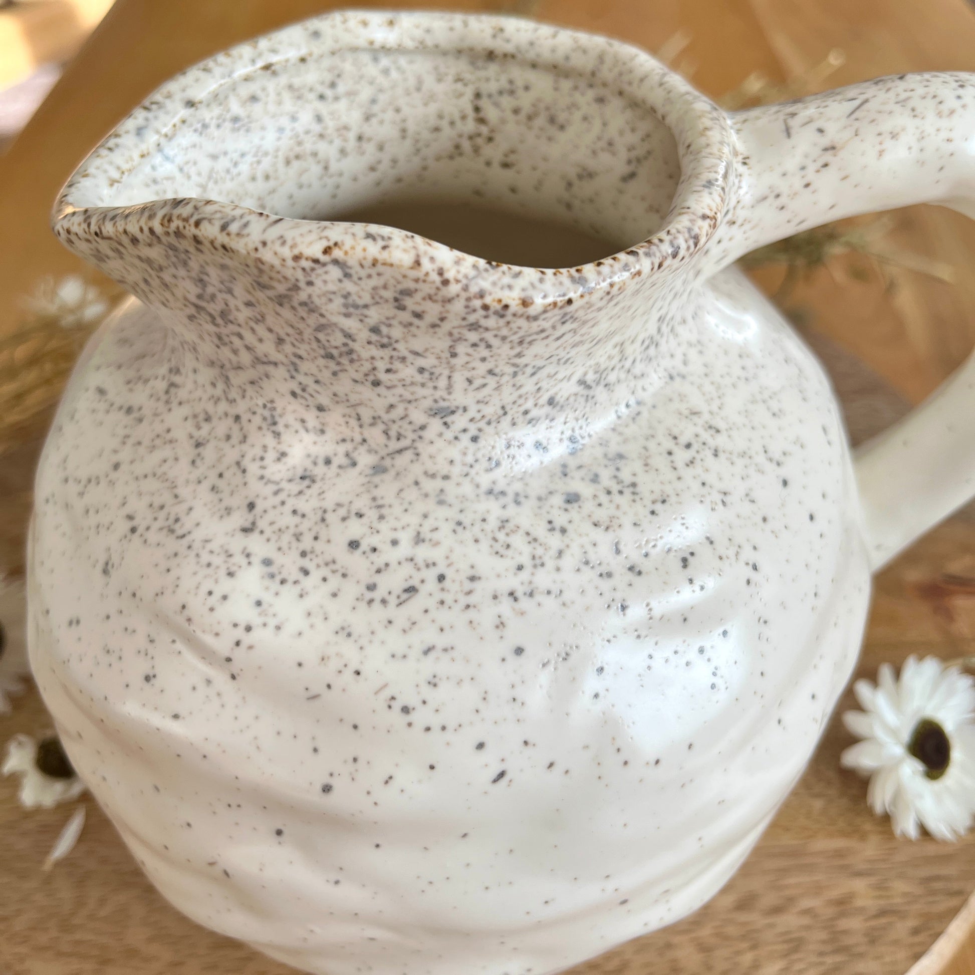 Speckled round ceramic jug on a wooden surface with a blurred background